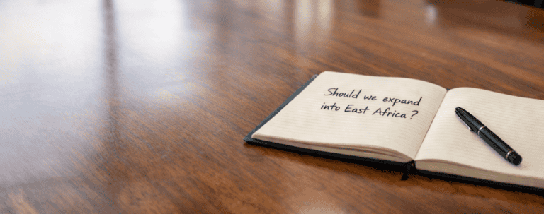 Open notebook on a wooden table with a pen, featuring the text "Should we expand into East Africa?"—a clear reminder of critical business decisions ahead.